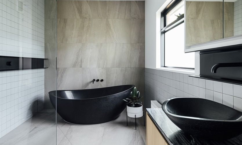 A black and white residential bathroom featuring a black freestanding bath and a black basin